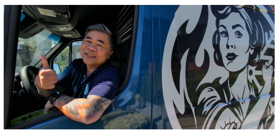 Venice Tabernero leaning out of a Mom’s Heating & Cooling van window giving a thumbs-up, with the Mom’s logo visible on the vehicle.